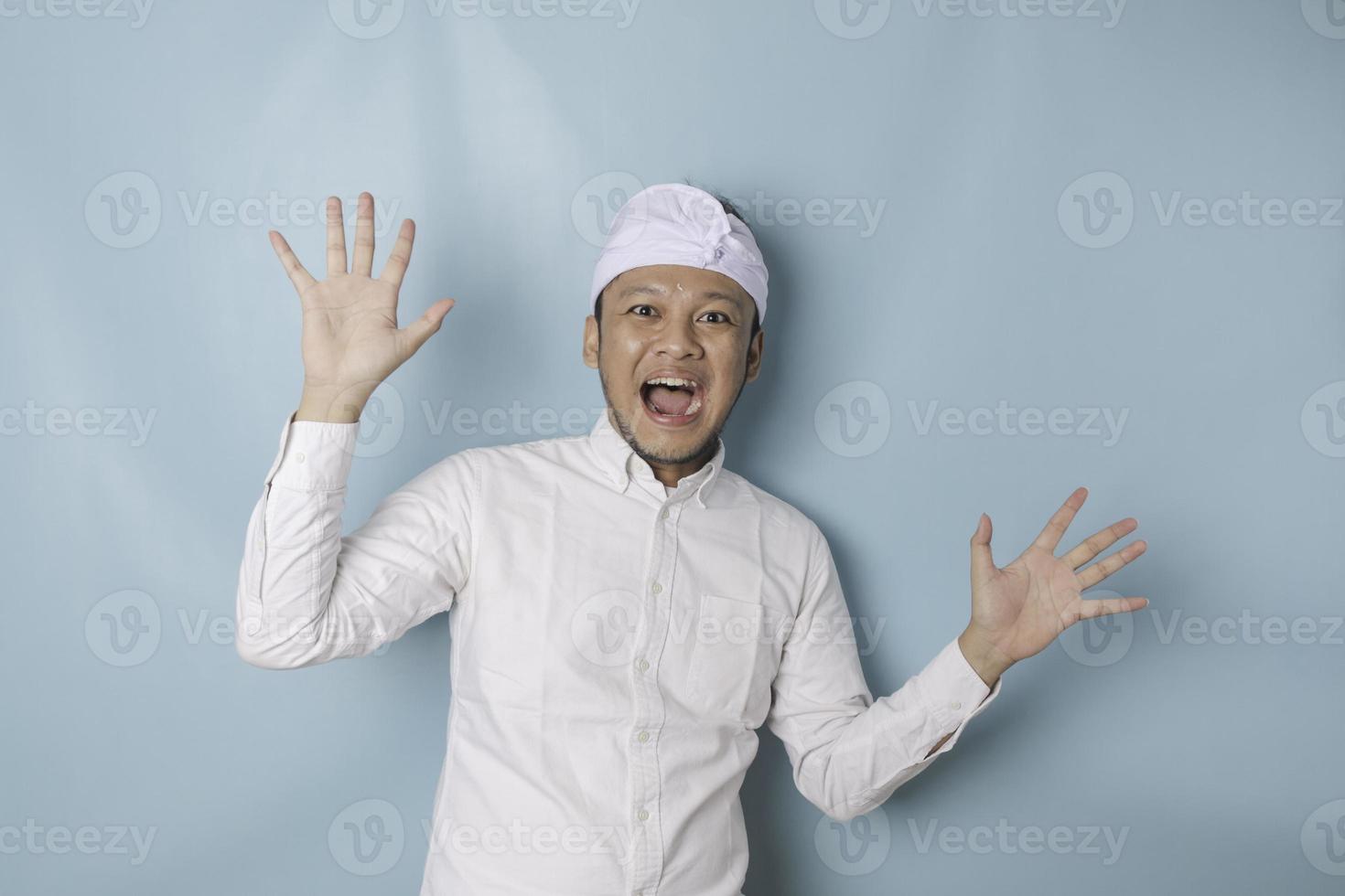 Surprised Balinese man wearing udeng or traditional headband and white shirt, isolated by blue background photo