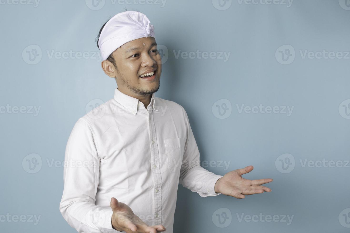 Young male doctor presenting an idea wearing udeng or traditional headband and white shirt while looking smiling on isolated blue background photo