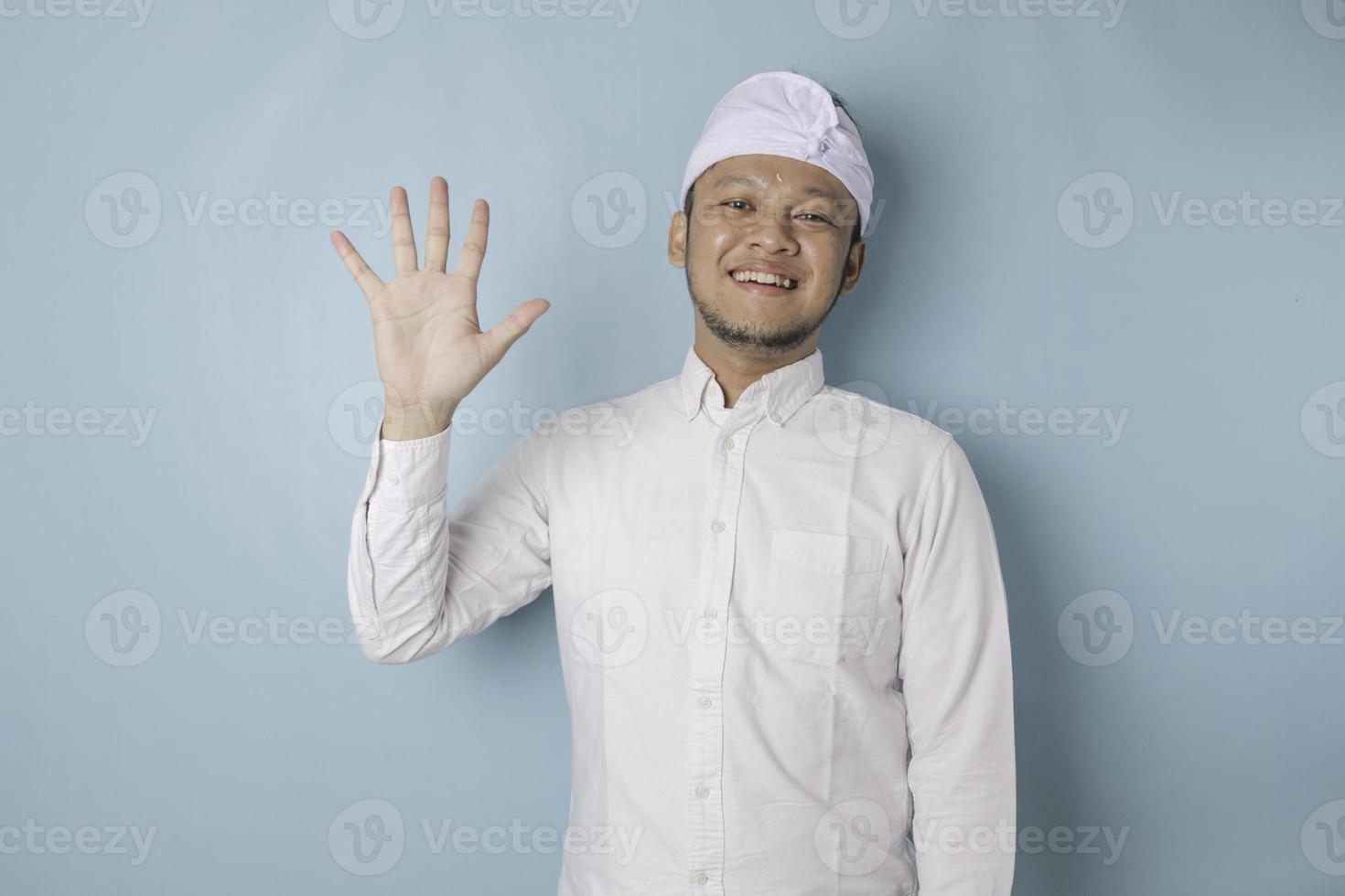 emocionado hombre balinés vestido con udeng o diadema tradicional y camisa blanca dando el número 12345 con gesto de mano foto