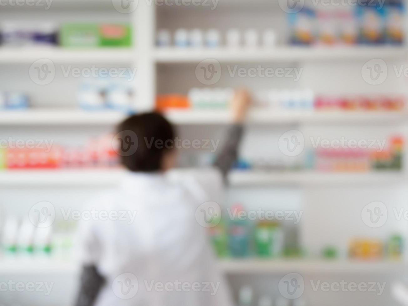 blur pharmacist taking medicine from shelf in pharmacy photo