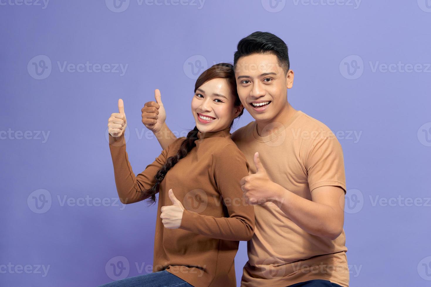 Happy young lovely couple showing thumbs up and looking at the camera over purple background photo