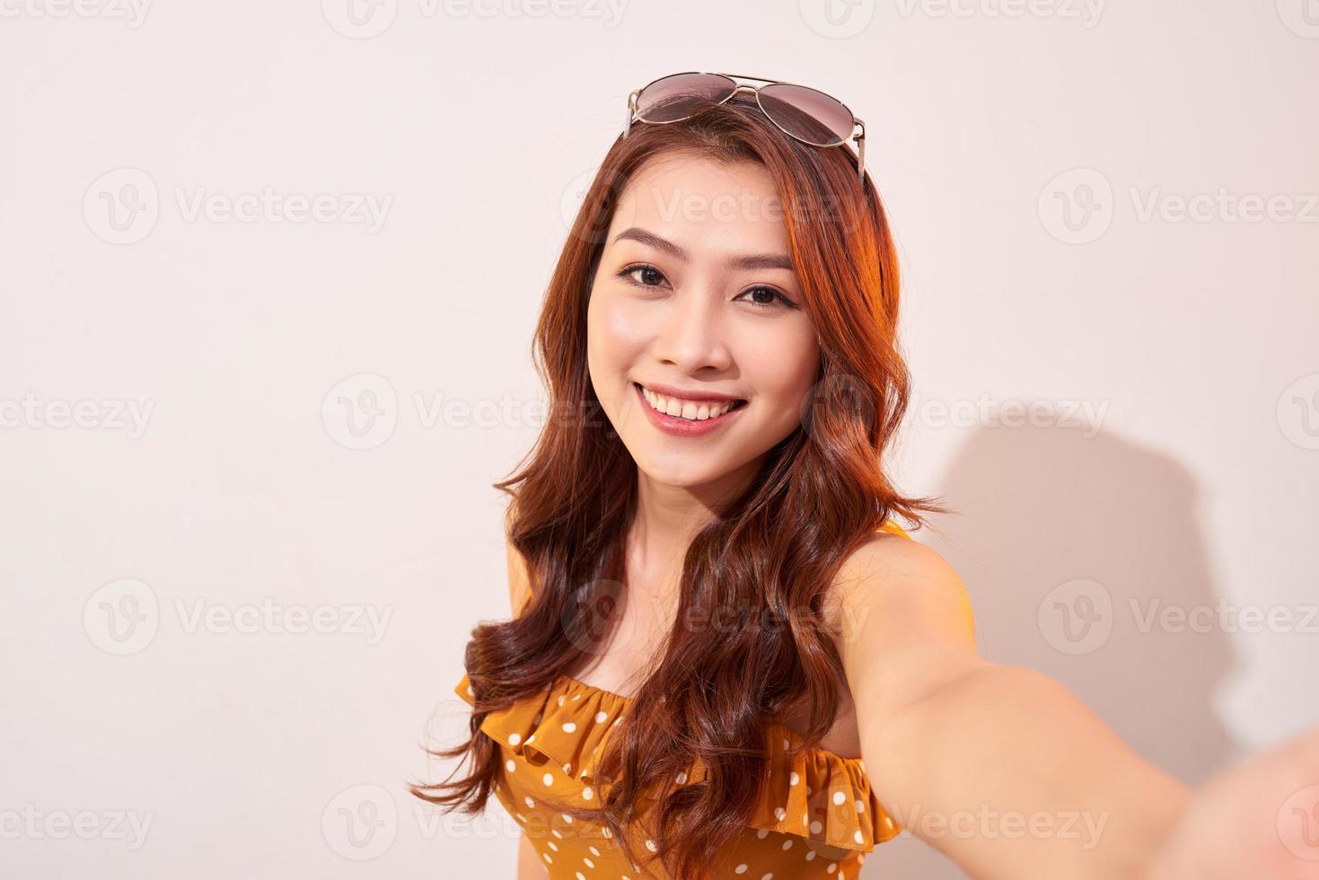 Carefree, careless concept. Young girl take selfie on front camera of modern smartphone wear in summer dress and beaming toothy smile isolated on shine beige background photo