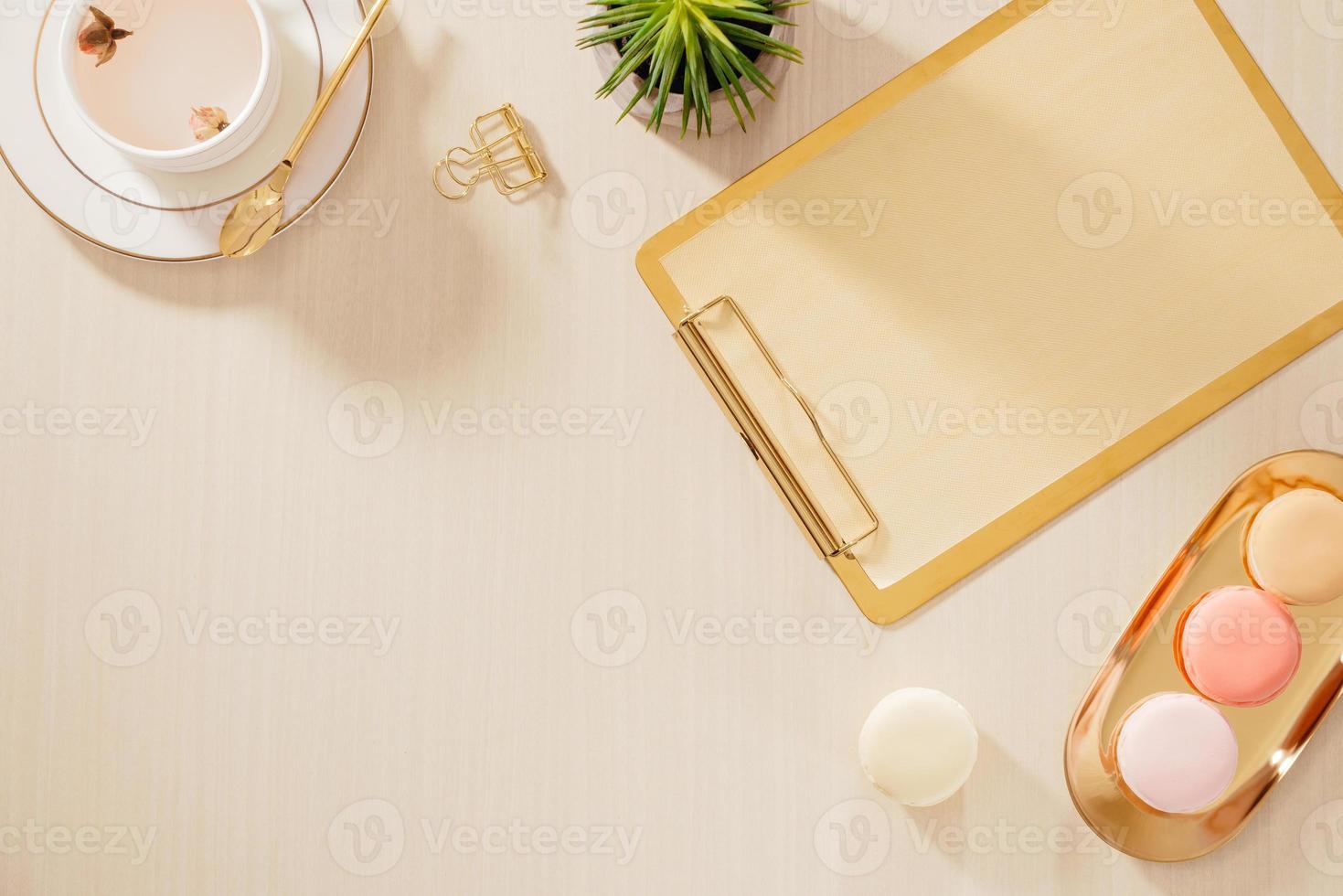 Modern gold stylized home office desk with folder, macaroons, coffee mug on beige background. Flat lay, top view lifestyle concept. photo