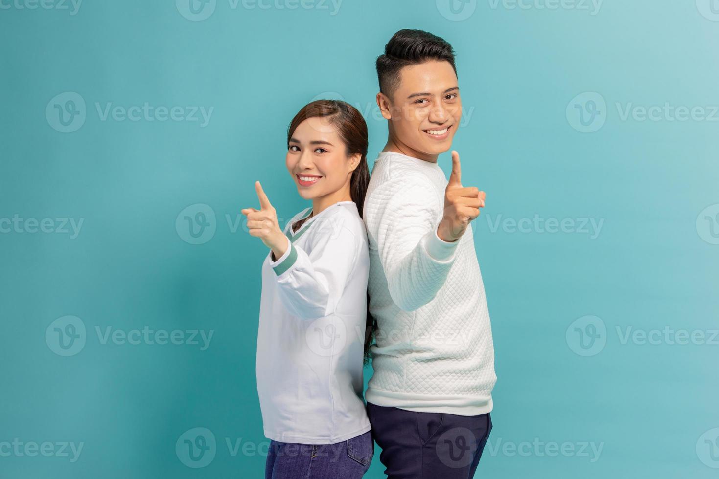 Portrait of happy young couple man and woman smiling and pointing fingers at camera isolated over blue background photo