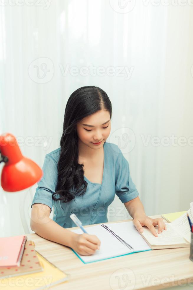 Teen girl preparing for test exam with laptop and books writing essay coursework in notebook studying at home photo