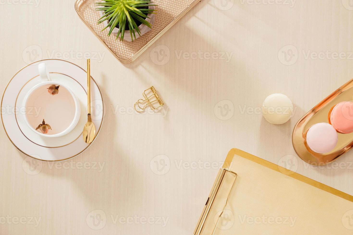 Modern gold stylized home office desk with folder, macaroons, coffee mug on beige background. Flat lay, top view lifestyle concept. photo