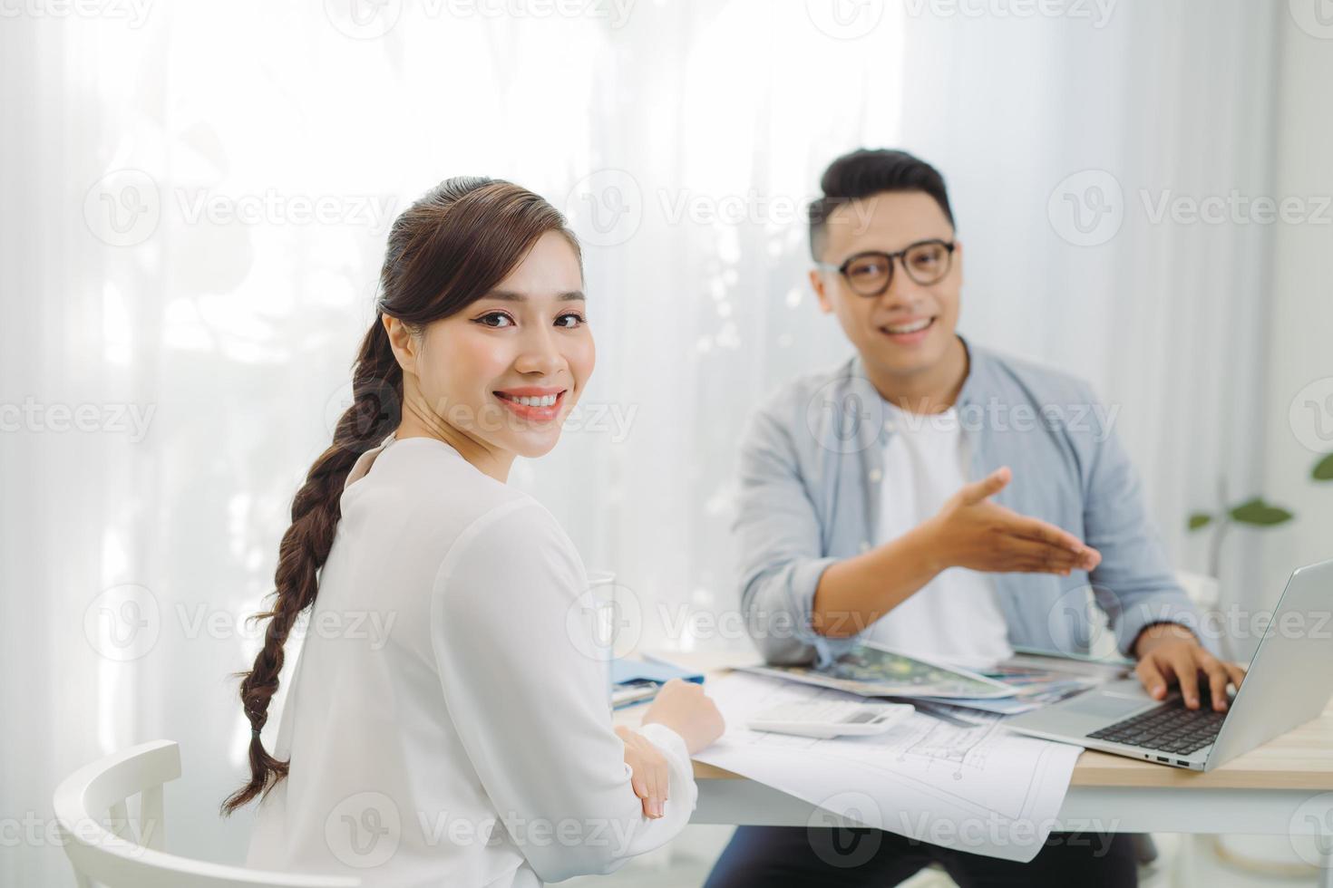 arquitecto masculino y femenino discutiendo un conjunto de planos repartidos en una mesa en la oficina. foto