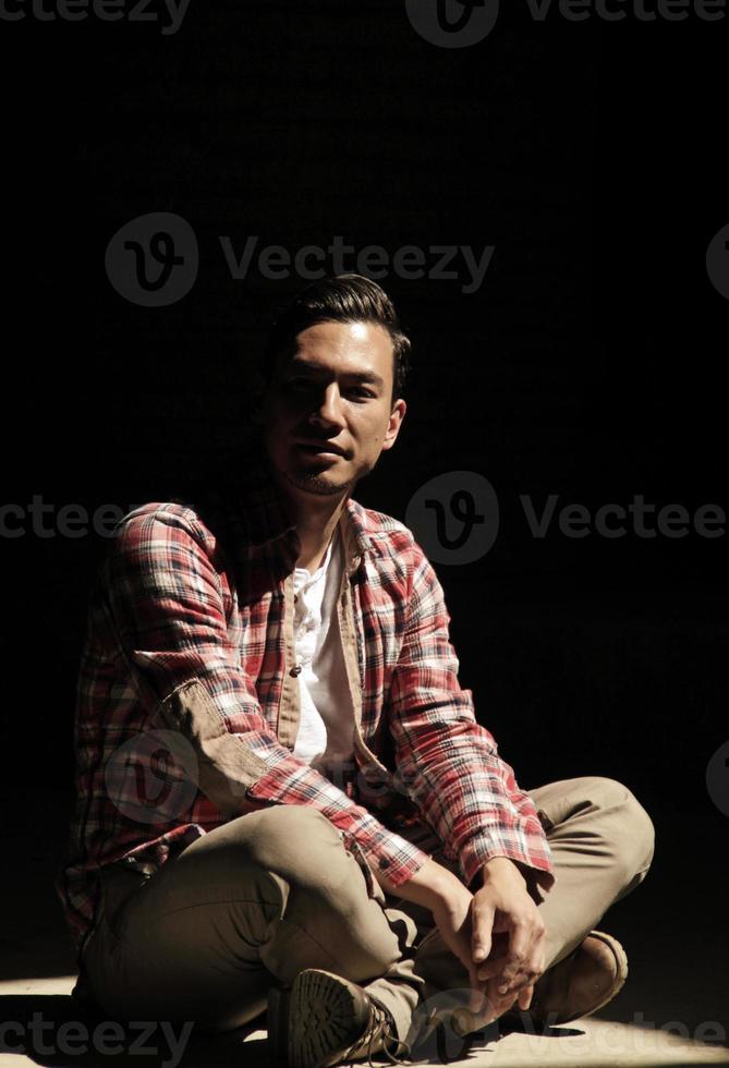 Handsome man with dark hair sitting on the floor in a spotlight photo