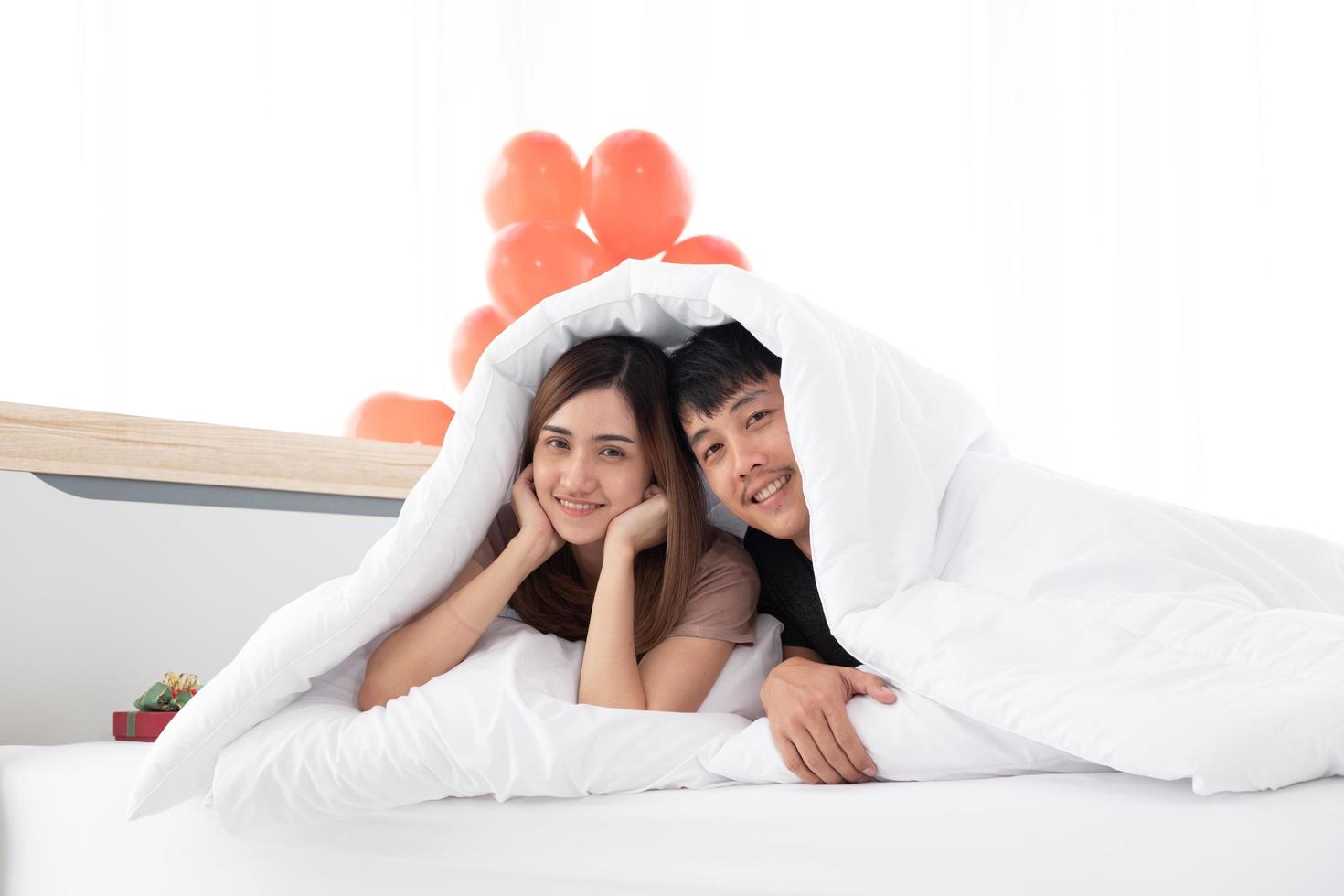 una feliz pareja joven está en la cama debajo de la manta después de despertarse en la mañana del día de san valentín en su dormitorio. foto