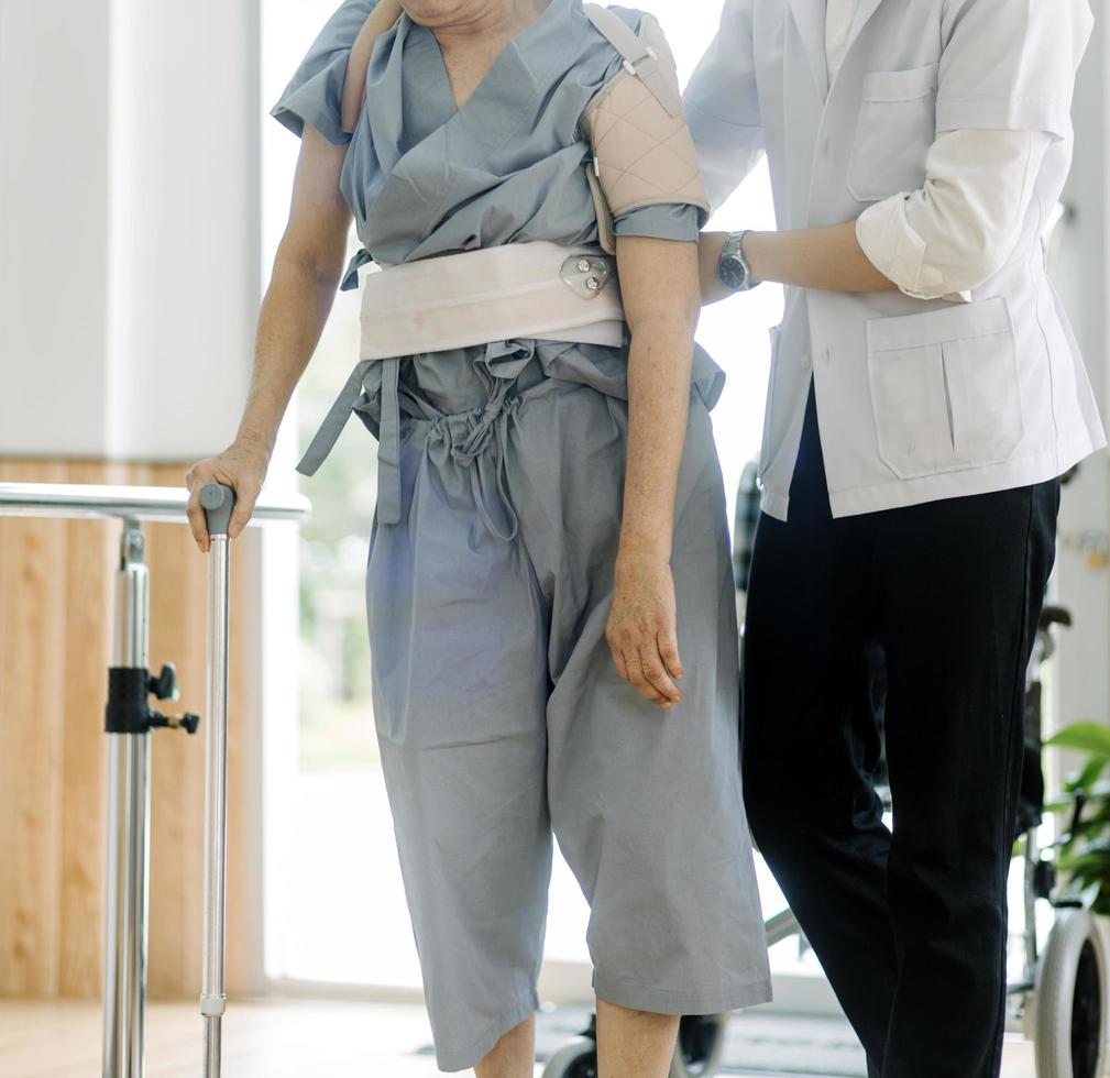 young asian physical therapist working with old man on working using a walker in hallway of nursing home photo