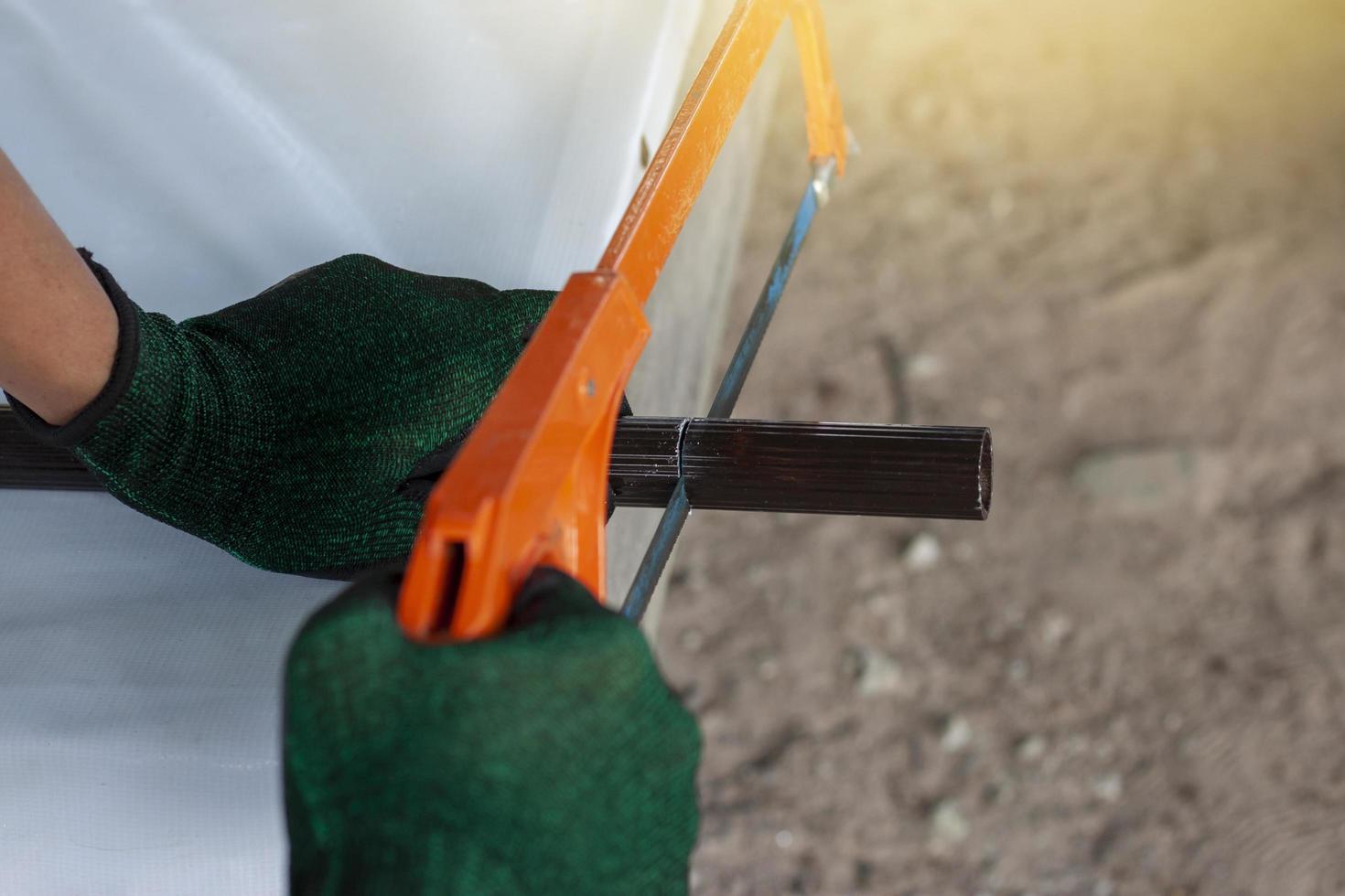 Hands of a construction worker wearing gloves is using a hacksaw to cut a piece of aluminum pipe. photo