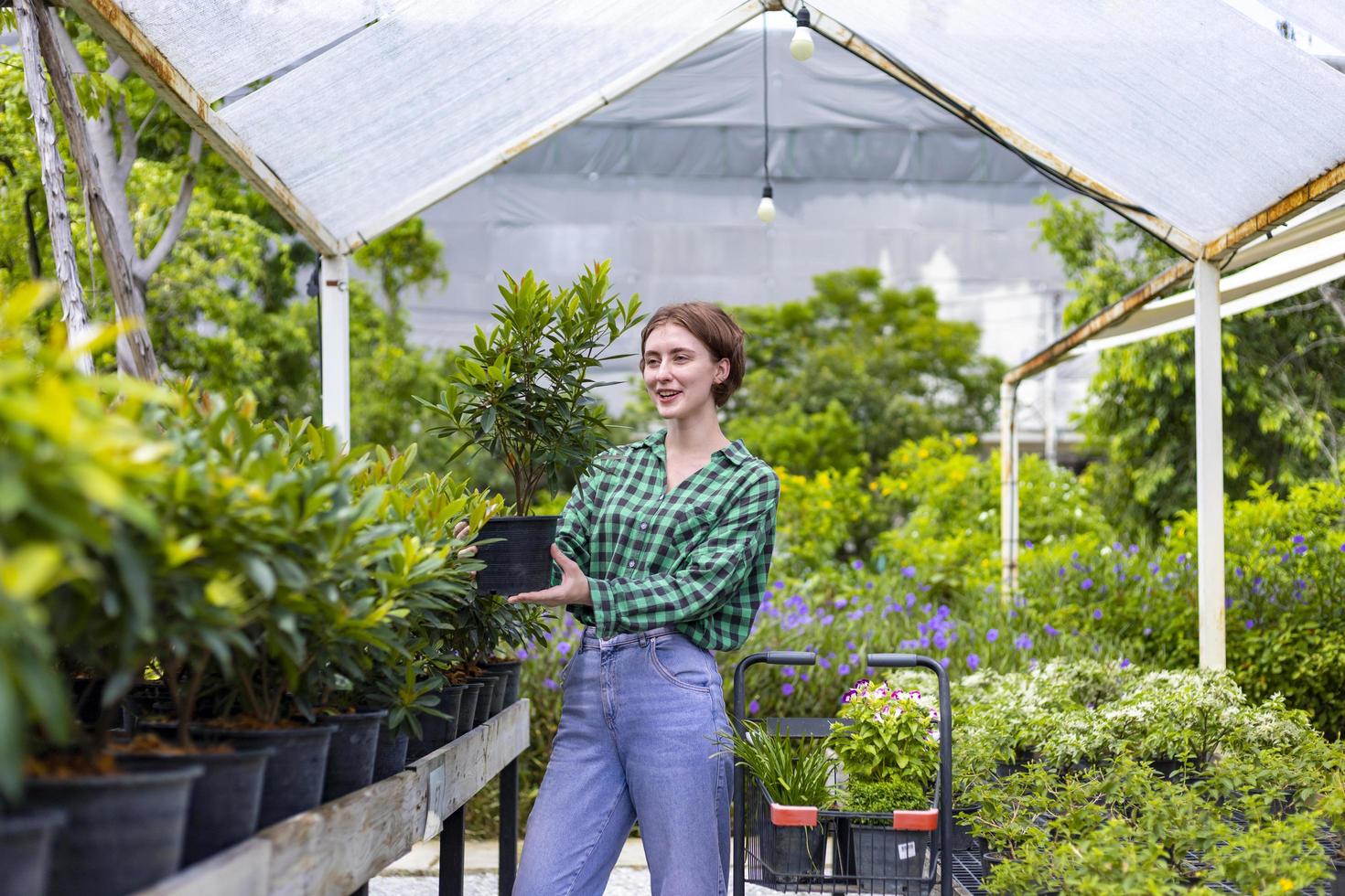 un joven cliente caucásico está eligiendo una planta exótica del vivero del centro de jardinería local con un carrito de compras lleno de plantas de verano para la jardinería de fin de semana y actividades al aire libre foto