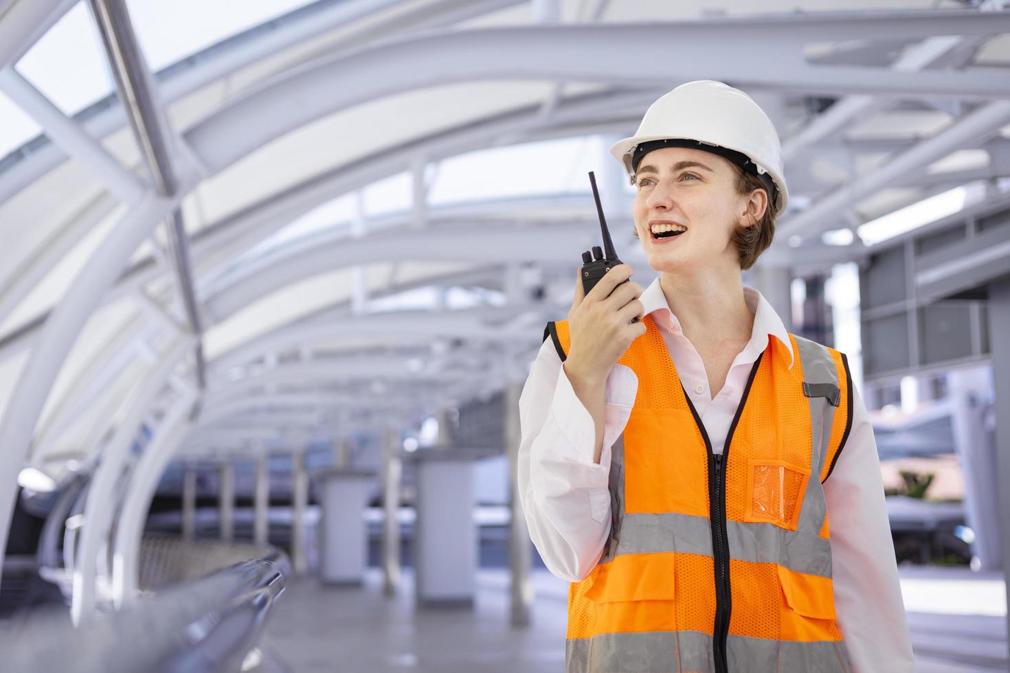 una ingeniera caucásica está usando walkie talkie mientras inspecciona el proyecto de construcción para la arquitectura moderna y el concepto de desarrollo inmobiliario foto