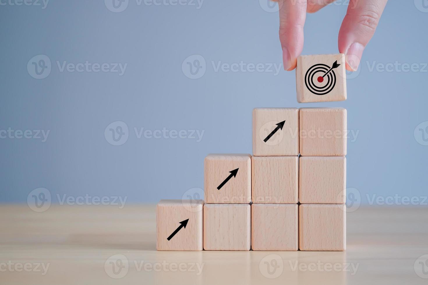 Business achievement goal and objective target. Growing business success concept. Hand holding wood block with dart board icon and arrow pointing to the target. photo