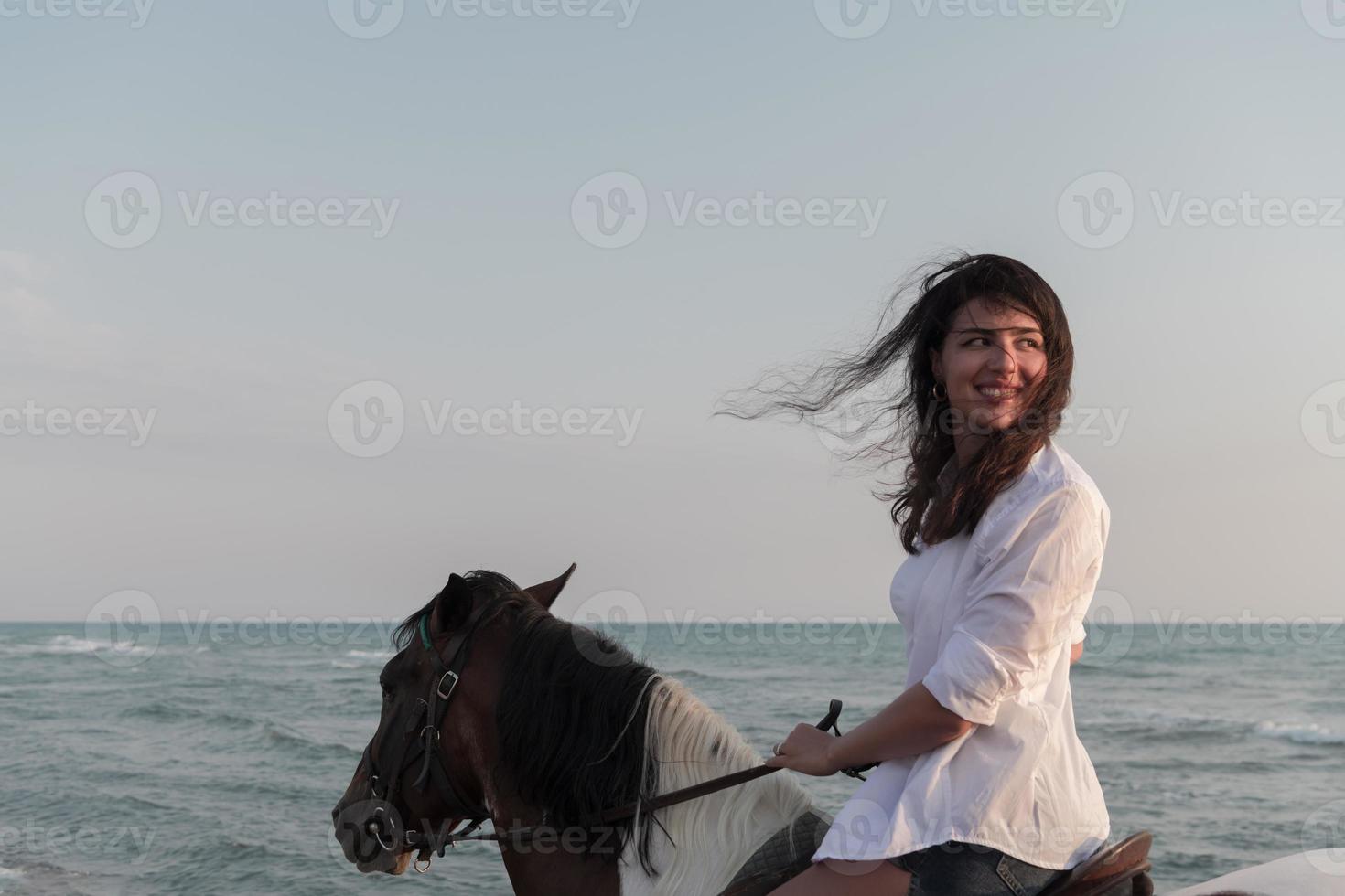 Woman in summer clothes enjoys riding a horse on a beautiful sandy beach at sunset. Selective focus photo