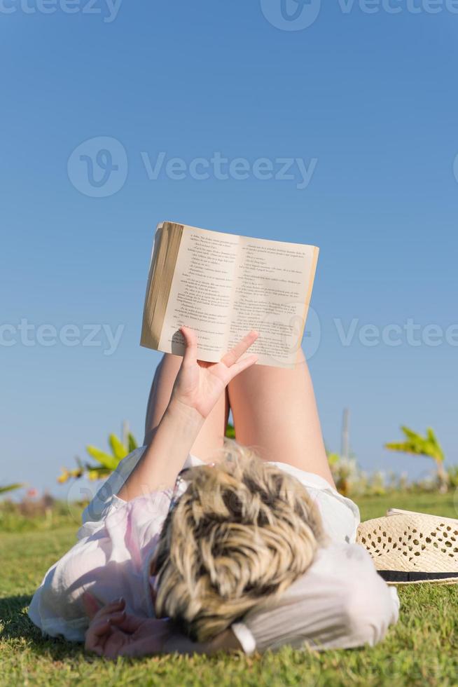 mujer acostada y leyendo su libro favorito en un prado cubierto de hierba verde fresca en un día soleado de verano o primavera. foto
