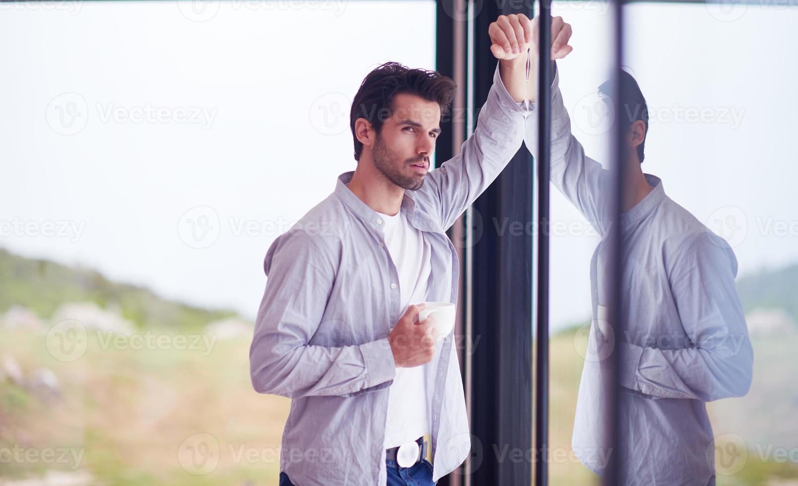 relaxed young man drink first morning coffee withh rain drops on window photo