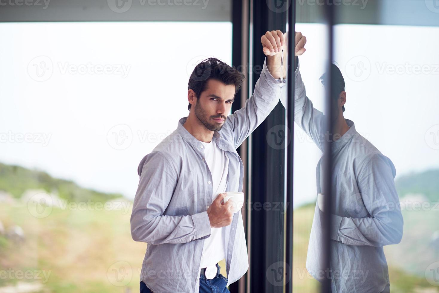 relaxed young man drink first morning coffee withh rain drops on window photo