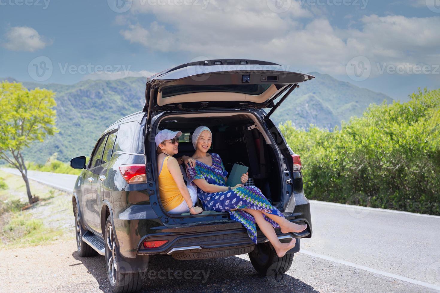 dos mujeres felices sentadas en el maletero del coche en un viaje por carretera. foto