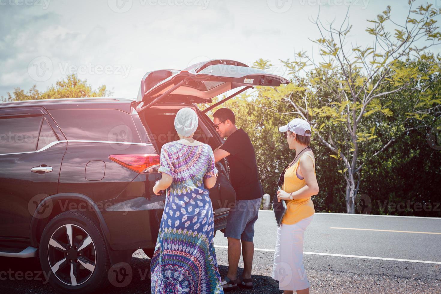 Man with female friends loading luggage in trunk of automobile on summer vacation trip photo