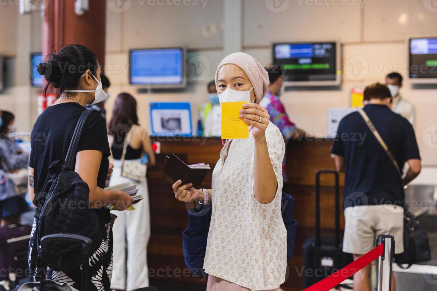 mujer asiática con máscara facial se registra en el aeropuerto y muestra su registro de vacunación. foto