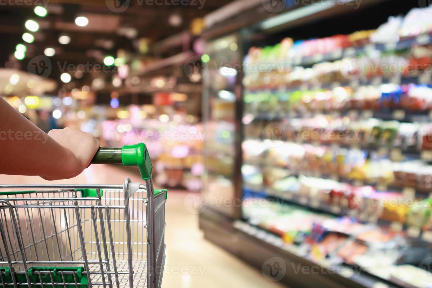 woman hand hold supermarket shopping cart with Abstract grocery store blurred defocused background with bokeh light photo