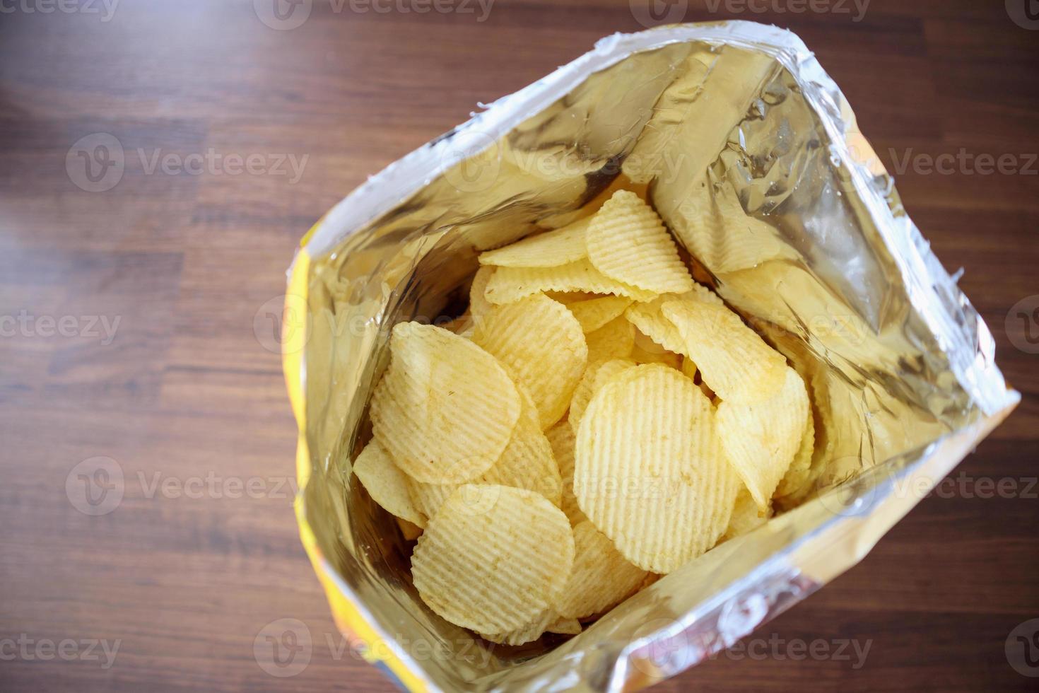 Potato chips in open snack bag close up on table floor photo