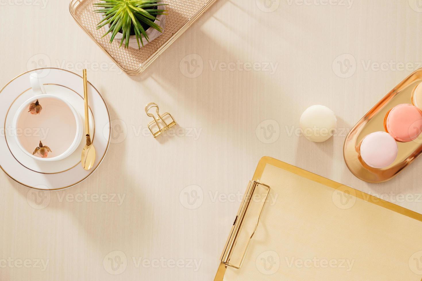 Modern gold stylized home office desk with folder, macaroons, coffee mug on beige background. Flat lay, top view lifestyle concept. photo