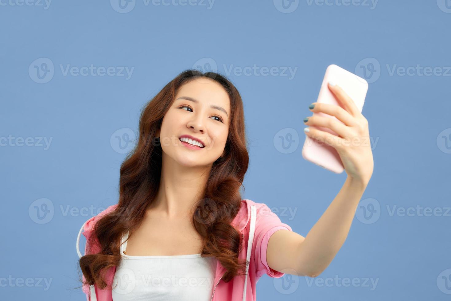 retrato de una chica alegre y fresca que tiene una videollamada con un amante sosteniendo un teléfono inteligente en la mano, disparando selfie en la cámara frontal aislada en un fondo azul. foto