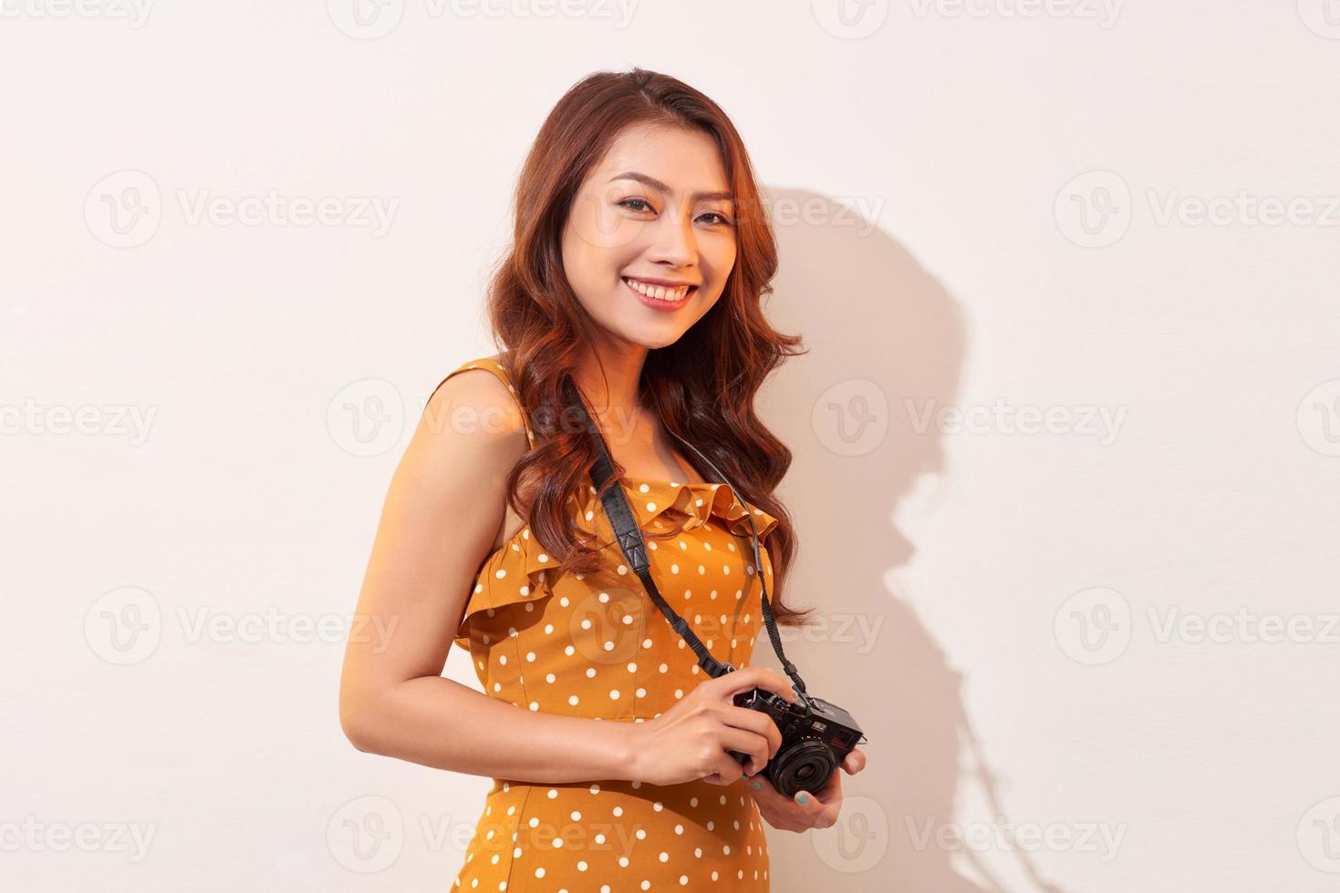 Portrait of cheerful smiling young woman taking photo with inspiration and wearing summer dress. Girl holding retro camera. Model posing on beige background in hat
