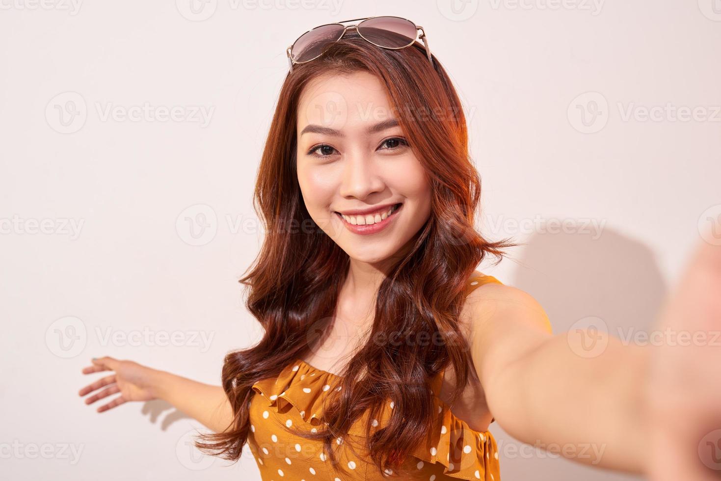 Carefree, careless concept. Young girl take selfie on front camera of modern smartphone wear in summer dress and beaming toothy smile isolated on shine beige background photo