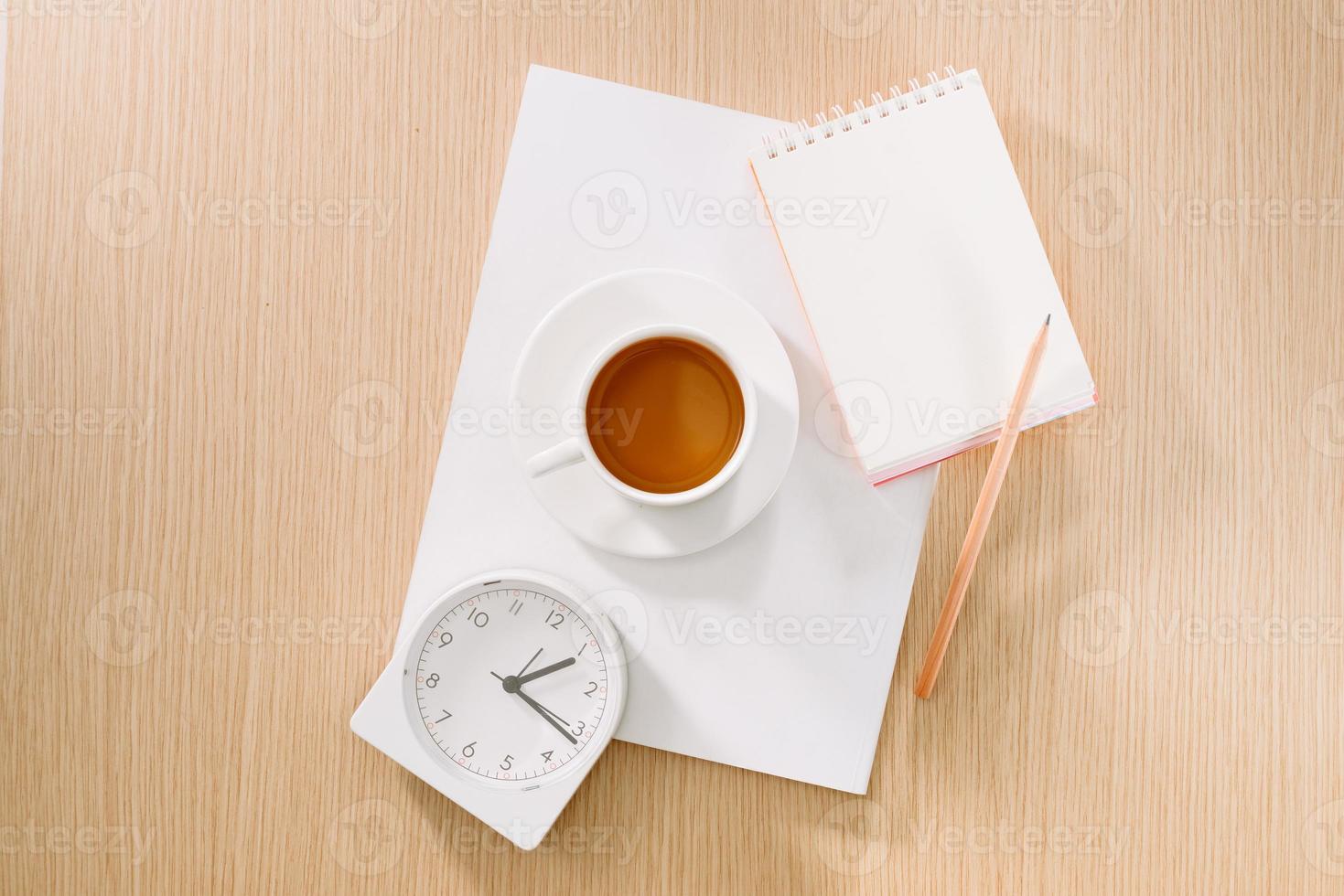 Flat lay of coffee cup, clock, pencil and a notebook. photo