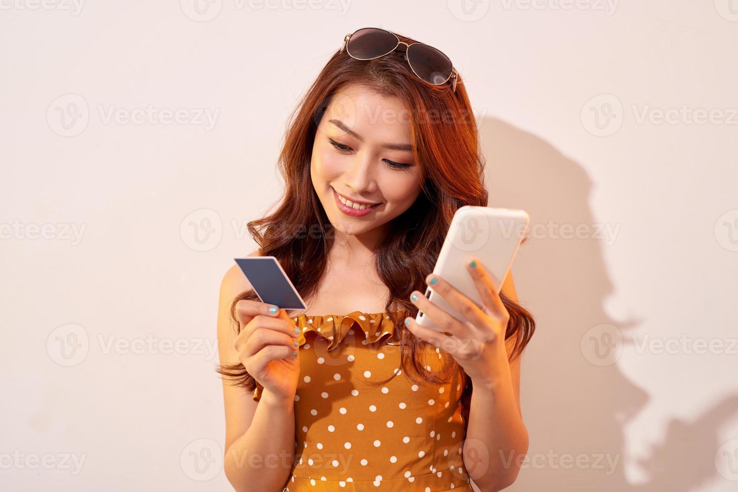 Image of excited young lady isolated over biege background using mobile phone holding credit card. photo