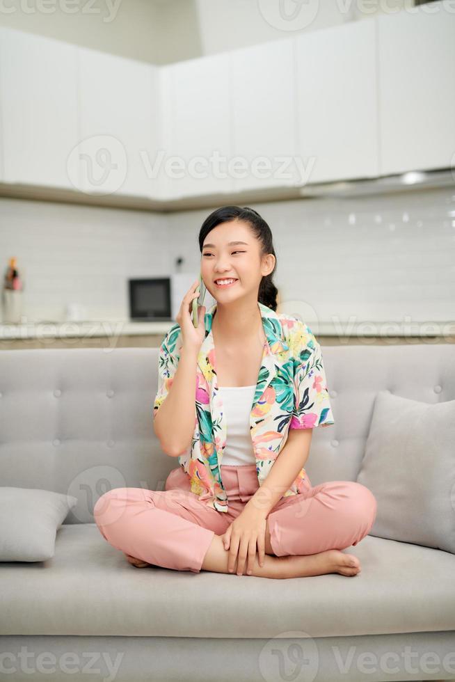 Happy young woman talking mobile phone while relaxing on couch photo