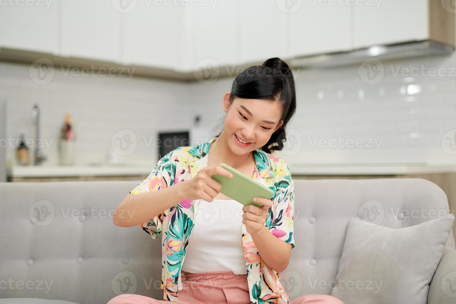 una mujer bonita juega al juego móvil por teléfono y se siente feliz en casa foto