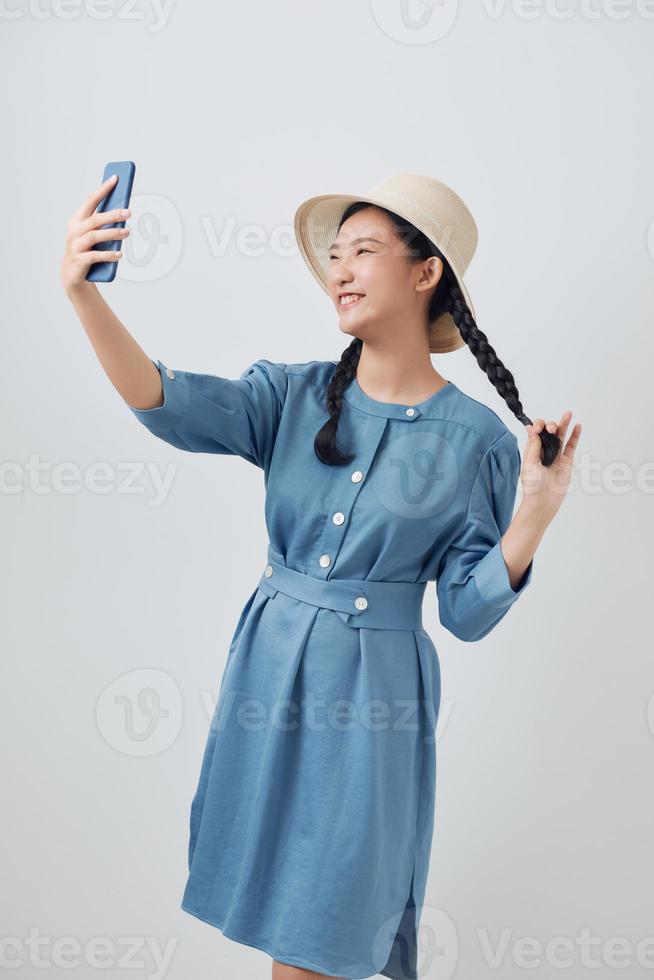 Happy beautiful girl in casual or hipster style, pigtail hairstyle, standing, holding mobile smart phone and doing selfie photo