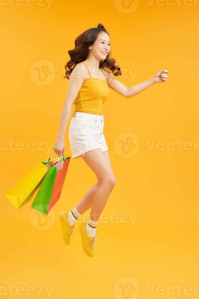 attractive happy woman jumping running holding shopping bags over orange background. Summer concept photo