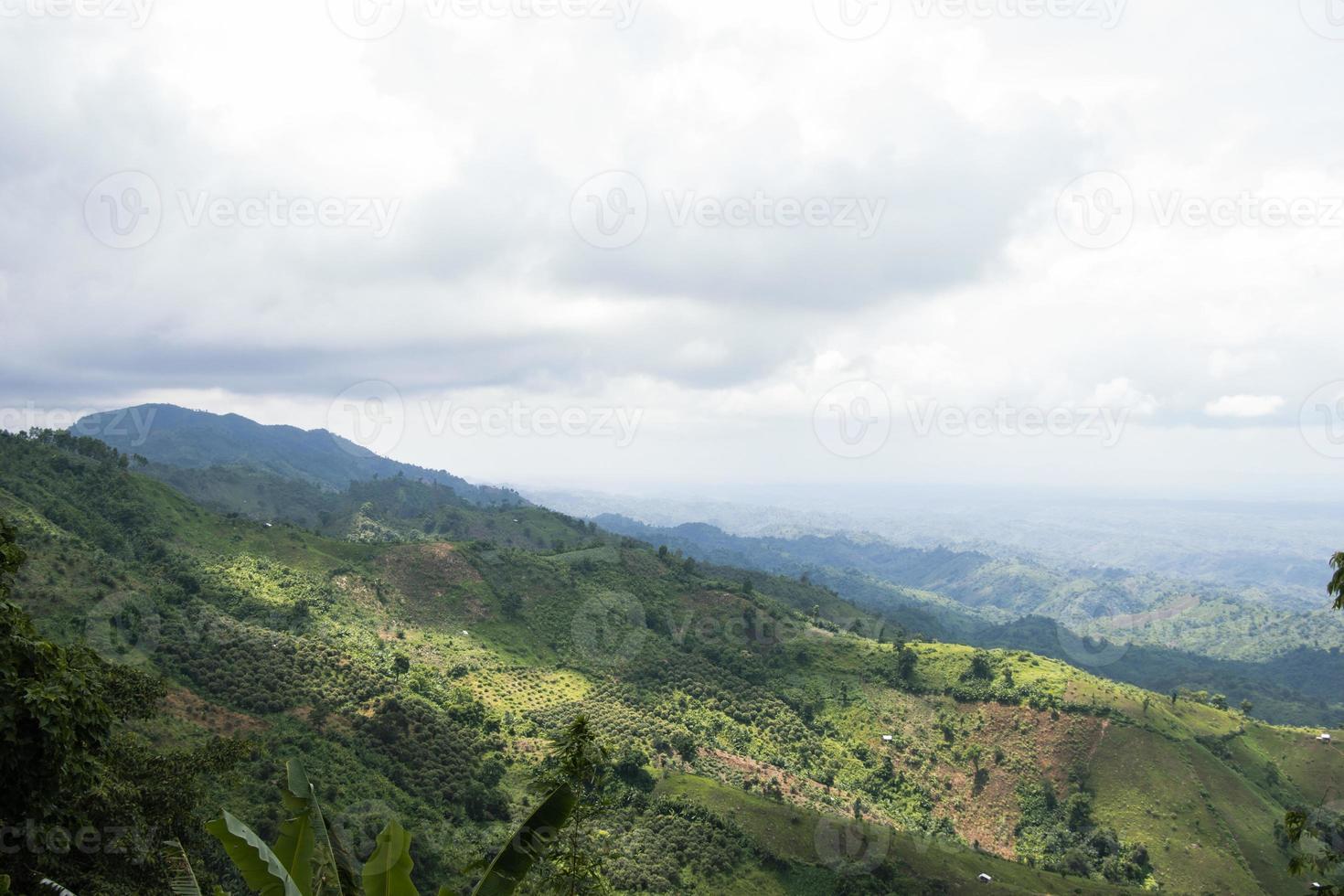 Rural mountain view with cloudy sky and hilly jungle. Green hilltop view with a drone. Hiking trail landscape photograph of hills. Beautiful hill station photo at Bandarban, Bangladesh.