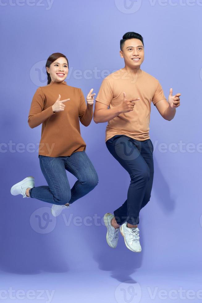 Great Offer. Positive couple jumping in air and pointing at copy space on purple background photo