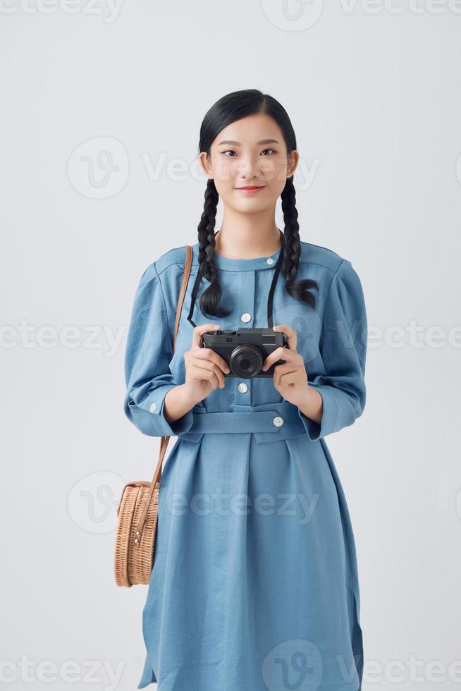 Smiling good looking Asian woman with long pigtail holds retro camera, takes pictures during her awesome trip photo