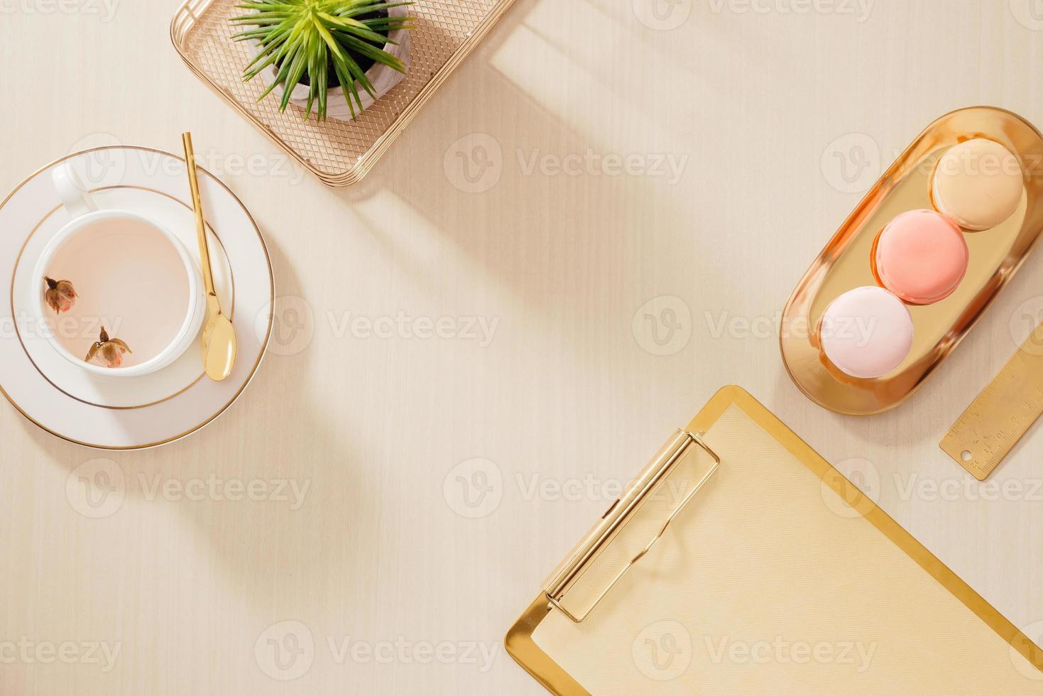 Modern gold stylized home office desk with folder, macaroons, coffee mug on beige background. Flat lay, top view lifestyle concept. photo