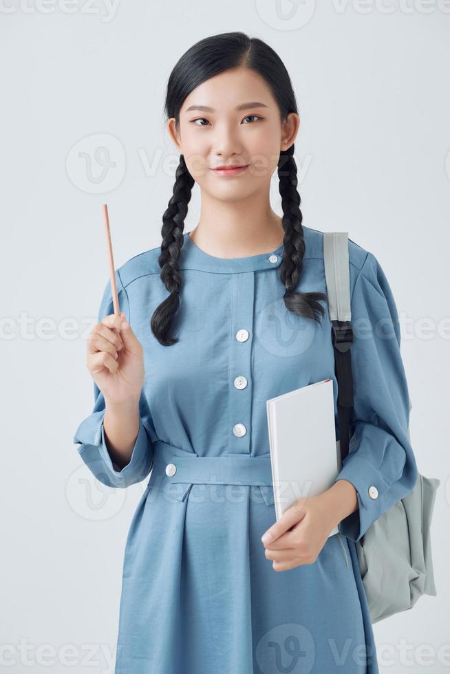 Cheerful young asian teen girl with backpack have an idea and holding notebook isolated on a white background photo