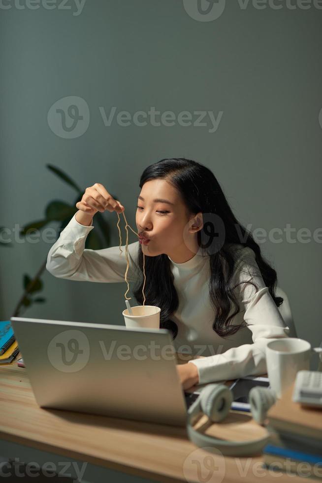 Asia freelance business woman eating instant noodles while working on laptop in living room at home office at night photo