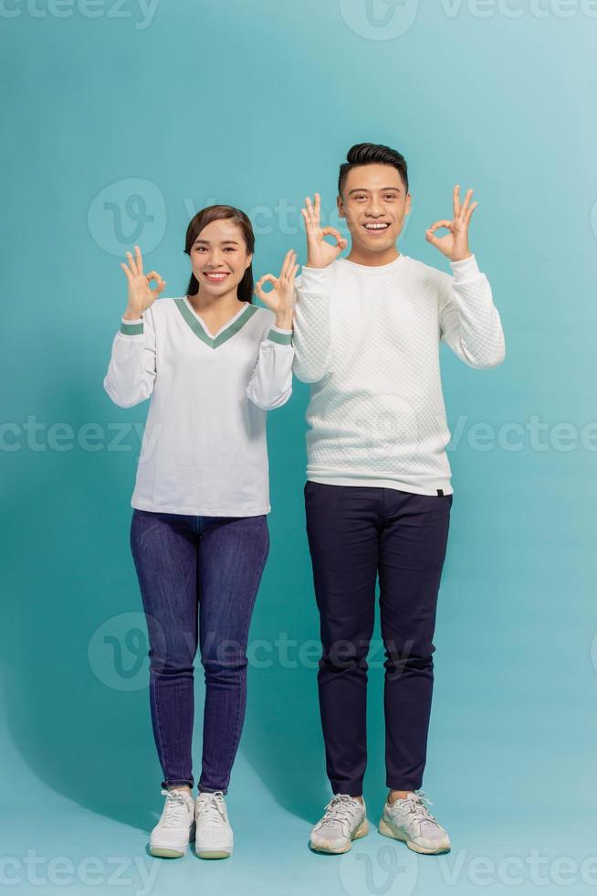Image of cheerful multinational man and woman smiling and gesturing ok sign isolated over blue background photo