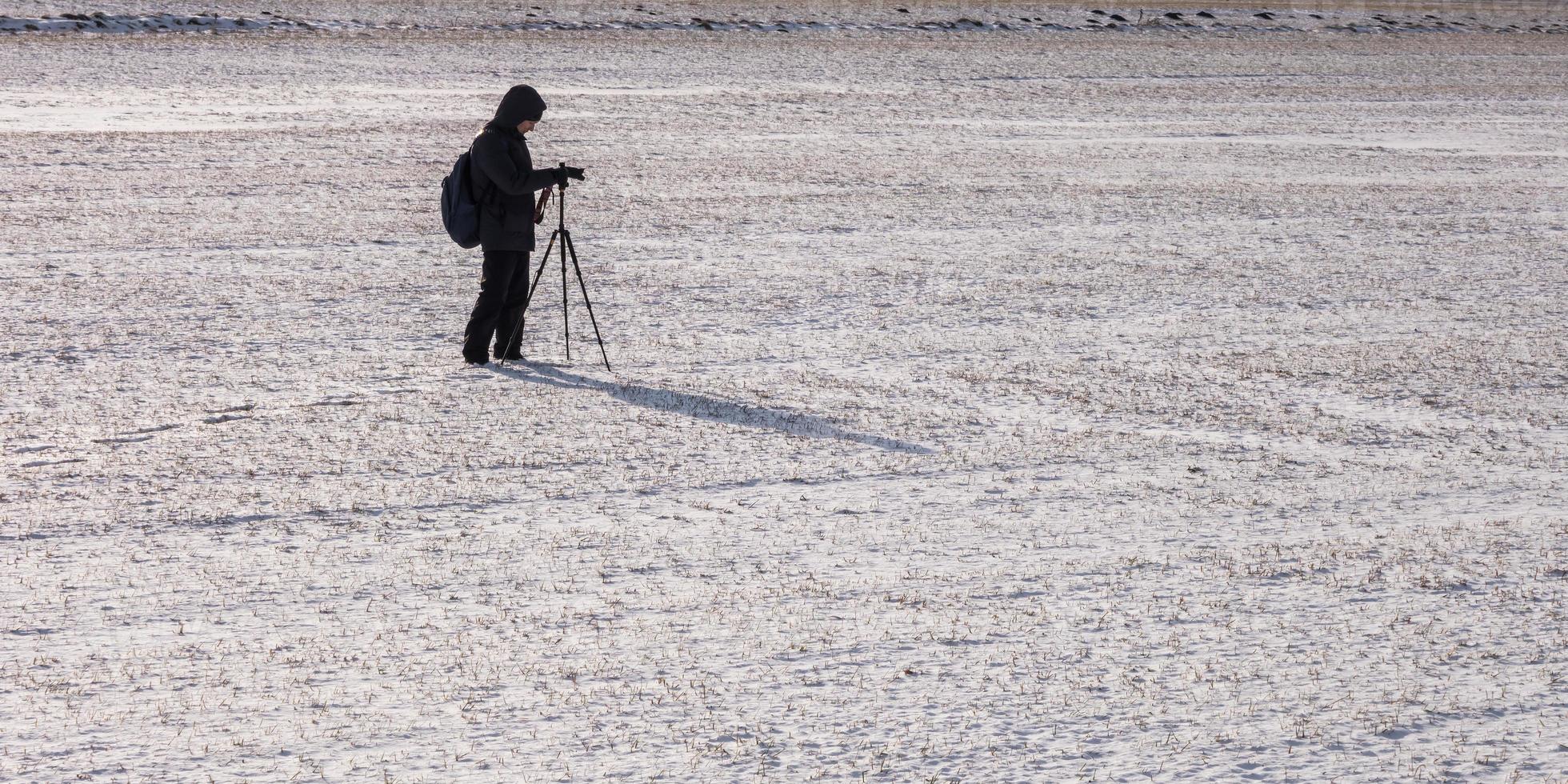 photographer with a tripod in snowy field takes pictures of winter landscape, footprints in snow photo