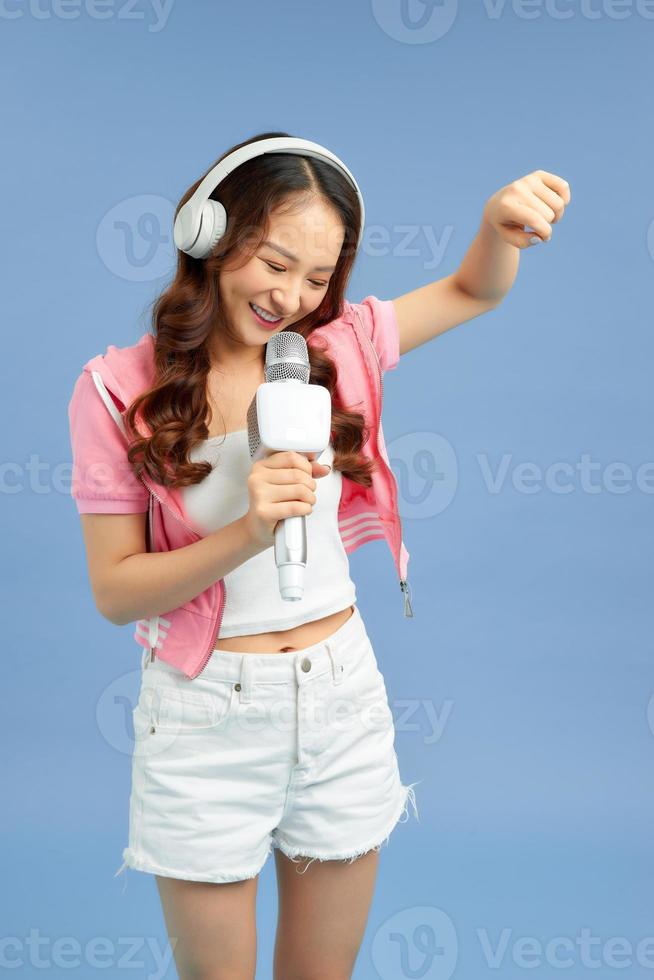 Beautiful young Asian woman singing into a microphone isolated over blue background. photo