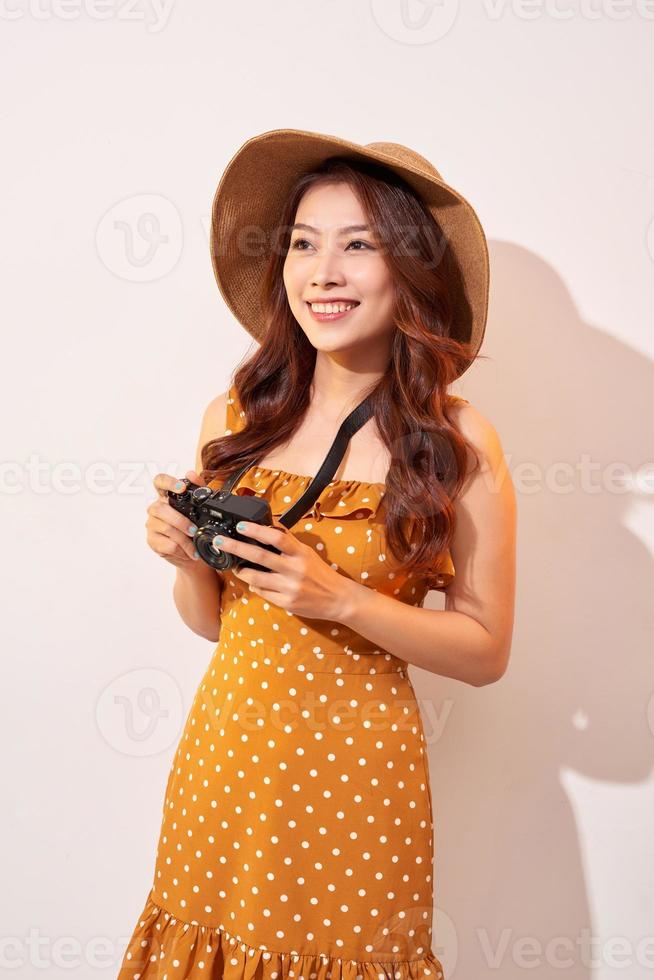 mujer joven atractiva con una cámara de fotos en la mano sobre un fondo beige aislado. el concepto de viaje