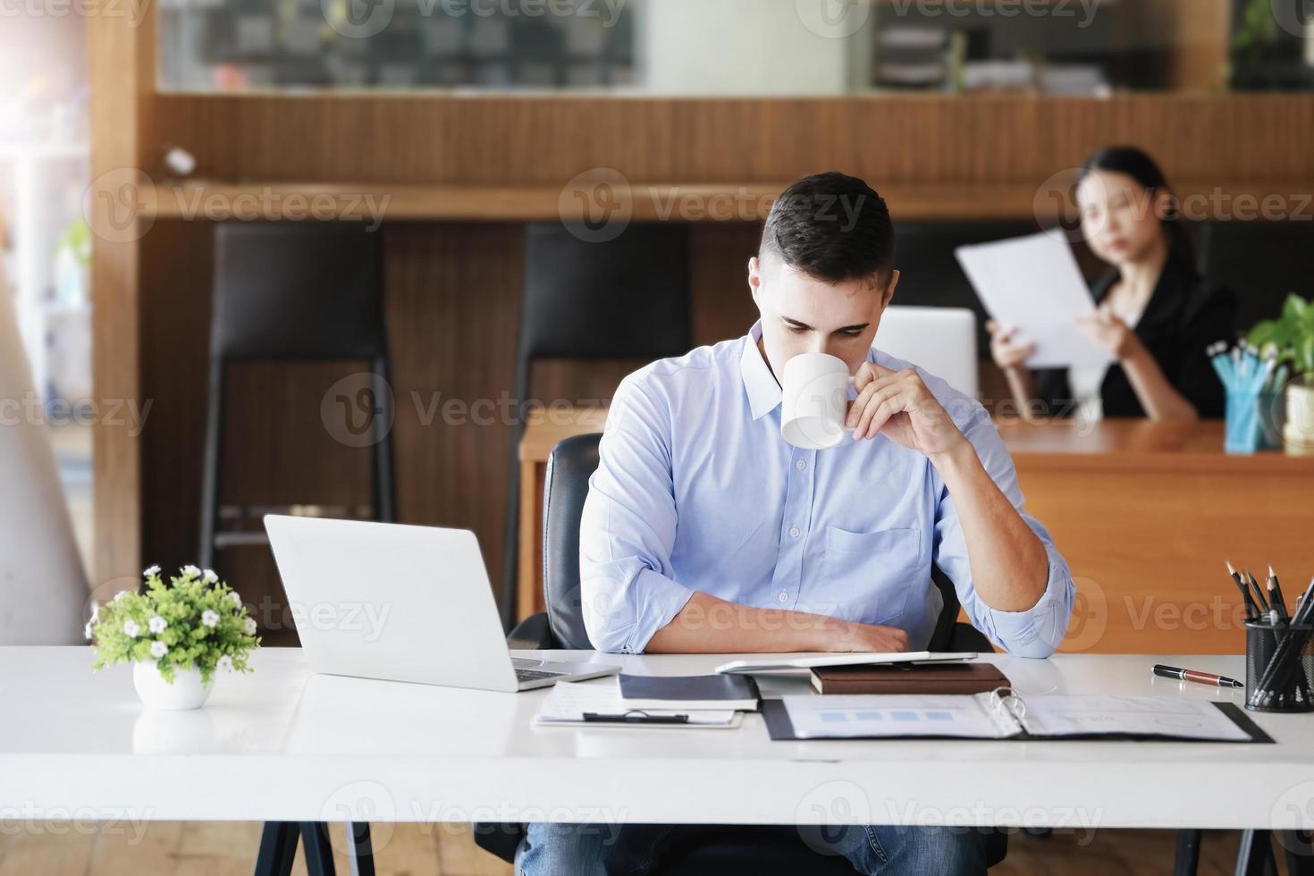 los gerentes de marketing masculinos toman café mientras trabajan para reducir la somnolencia antes de usar computadoras, ipads y documentos de análisis de marketing. foto