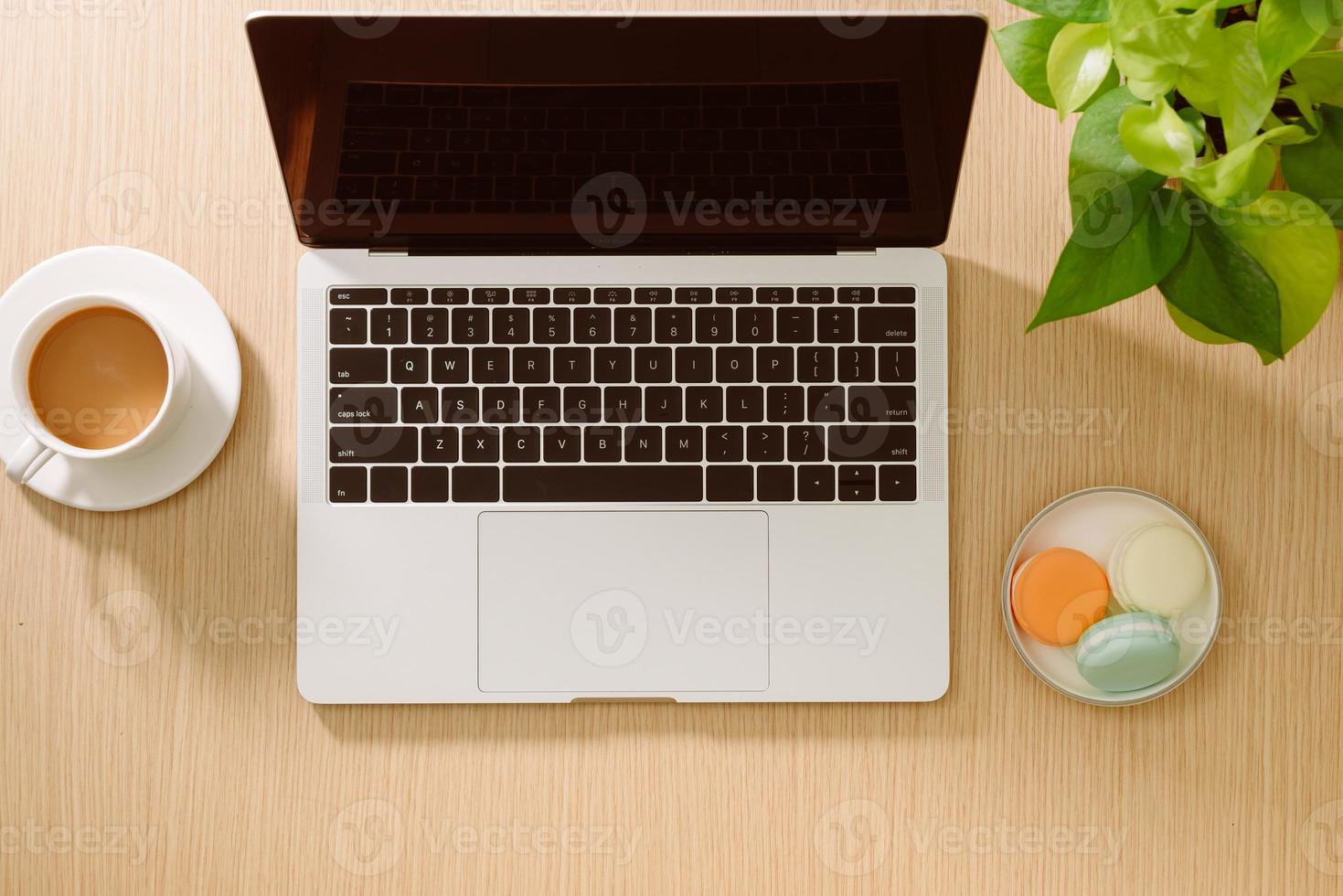 Laptop, colored macaroons cookies, cup of coffee with notebook on wooden table. Top view. Flat lay photo