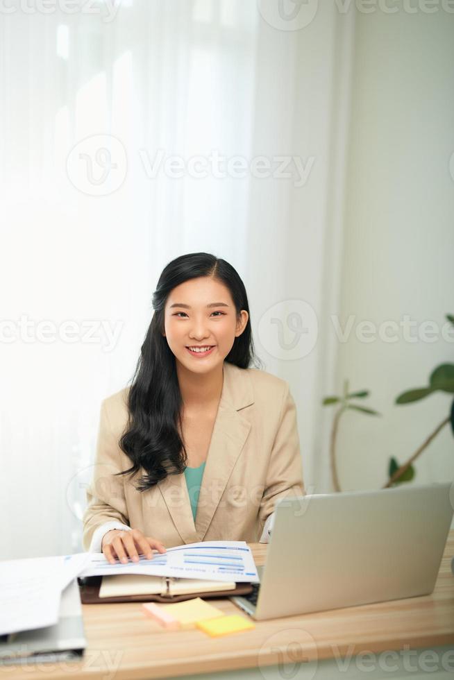 imagen de una joven complacida, feliz, alegre, linda, hermosa mujer de negocios sentada en el interior de la oficina usando una computadora portátil foto